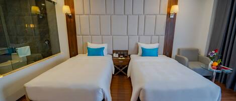 Een hotelkamer met twee bedden, een houten hoofdbord, een klein tafeltje met een telefoon en een lamp, en een glazen scheidingswand.
