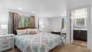 A bedroom with a large bed, bedside tables, a nightstand, a chair, a vanity with a mirror, and a window with curtains. - Beach, harbor & restaurants within walking distance. Family friendly home! (Sturgeon Bay)
