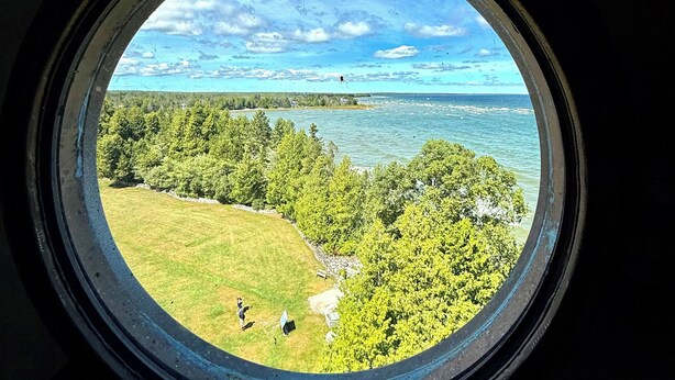 A circular window with a view of a grassy area, trees, and a body of water. - Beach, harbor & restaurants within walking distance. Family friendly home! (Sturgeon Bay)