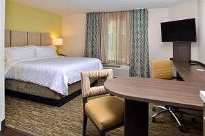 A hotel room with a bed, a desk, a chair, a television, and a patterned curtain. - Candlewood Suites Lodi (Lodi)