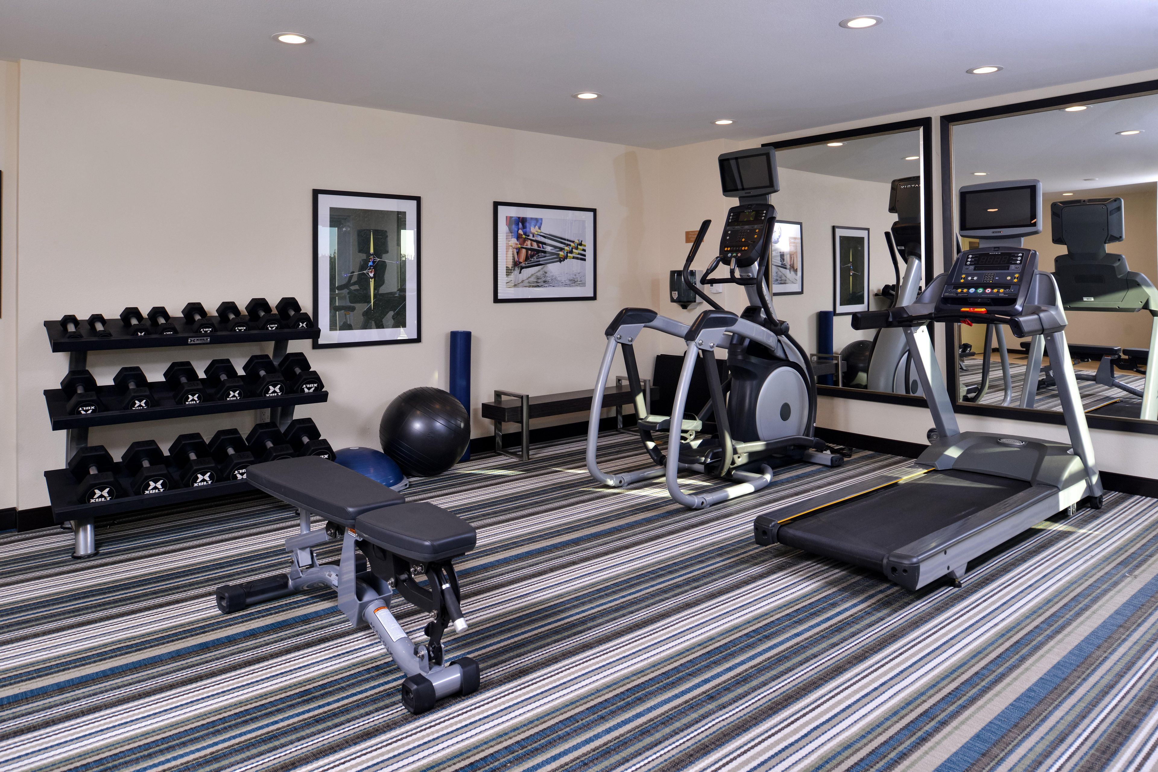 A gym with treadmills, a bench, dumbbells, and exercise balls.