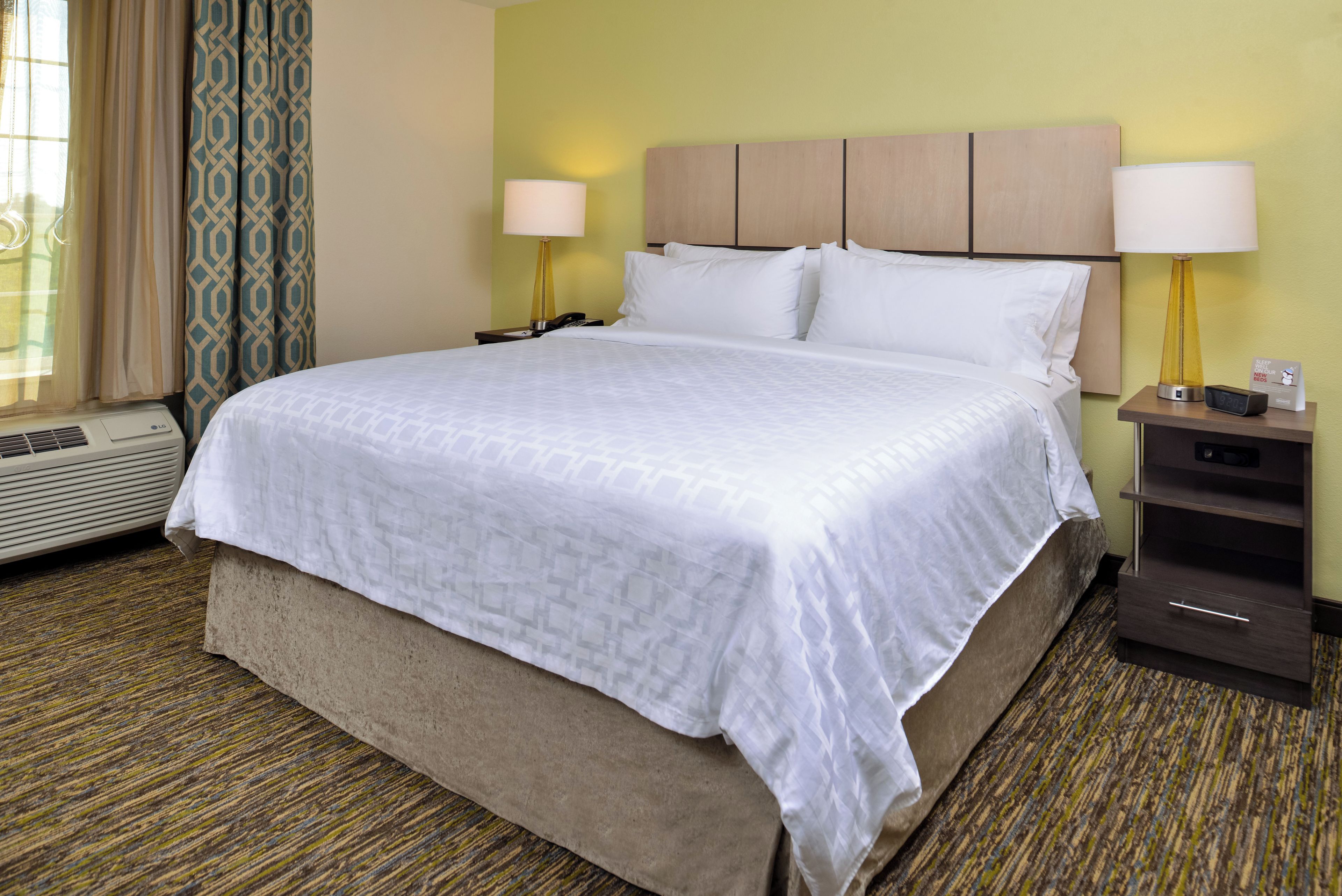 A hotel room with a large bed, two bedside lamps, a nightstand, a heater, and a patterned carpet.