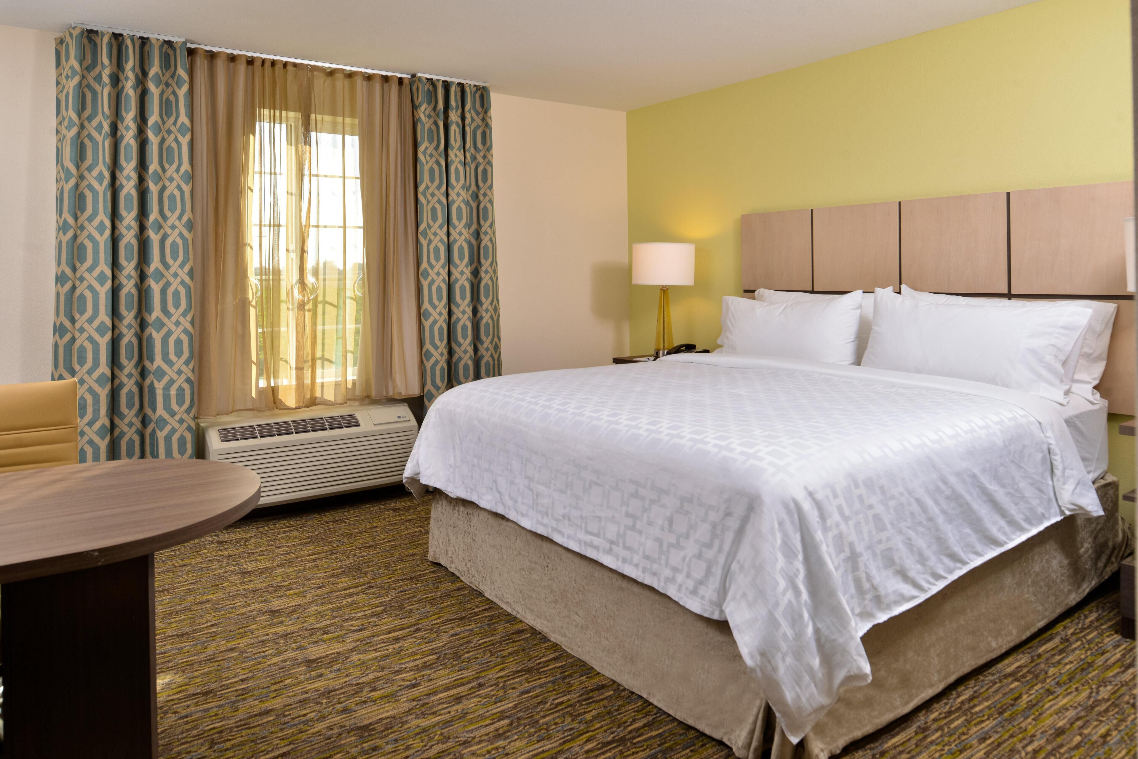 A hotel room with a bed, a desk, a lamp, and a window with curtains.