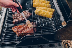 Una parrilla con carne y mazorcas de maíz.