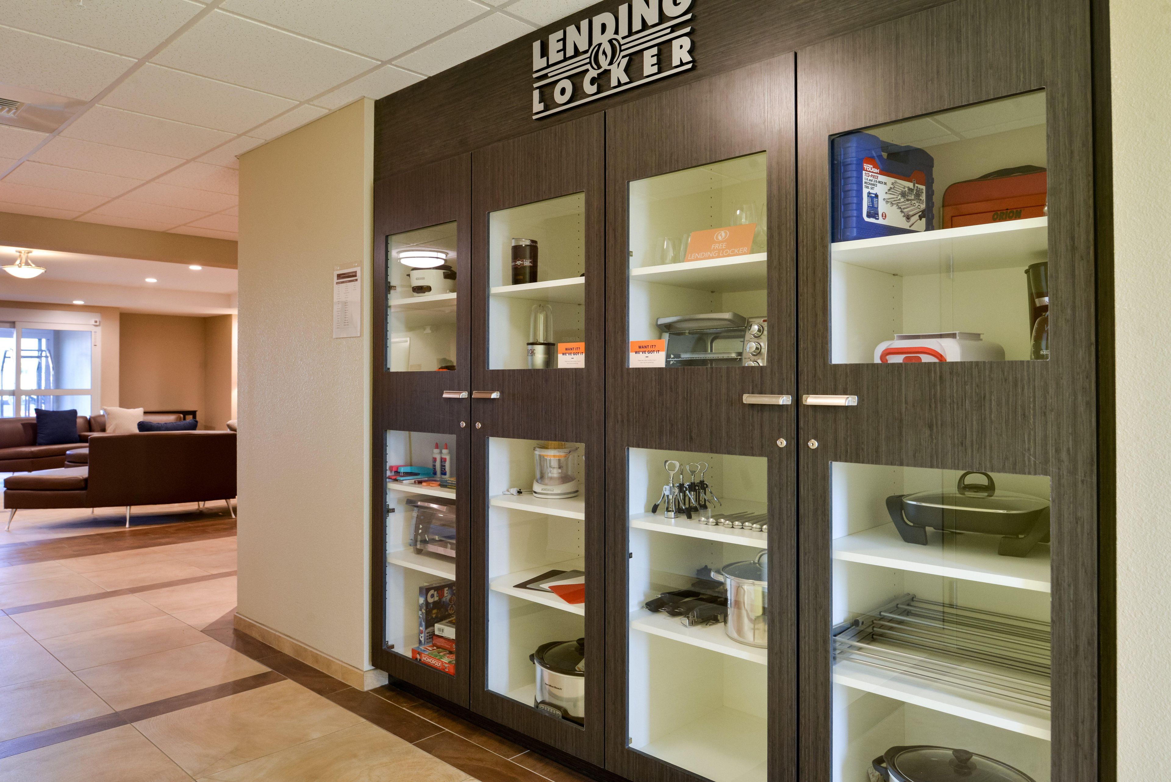 Una hall d'albergo moderna con un'area deposito che include porte in vetro, scaffali con utensili da cucina e un angolo relax con divano e tavolino.