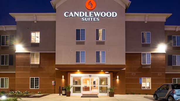 Entrada de hotel con diseño moderno, que presenta un logotipo destacado sobre el nombre, un acceso cubierto y un área de estacionamiento al frente.