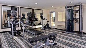 Un gimnasio con cintas de correr, elípticas, un banco y una estructura para sentadillas.