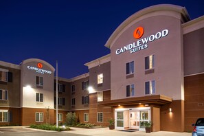 Un hotel de varios pisos con un llamativo letrero de "Candlewood Suites", que presenta un diseño moderno con una entrada curva y múltiples ventanas.