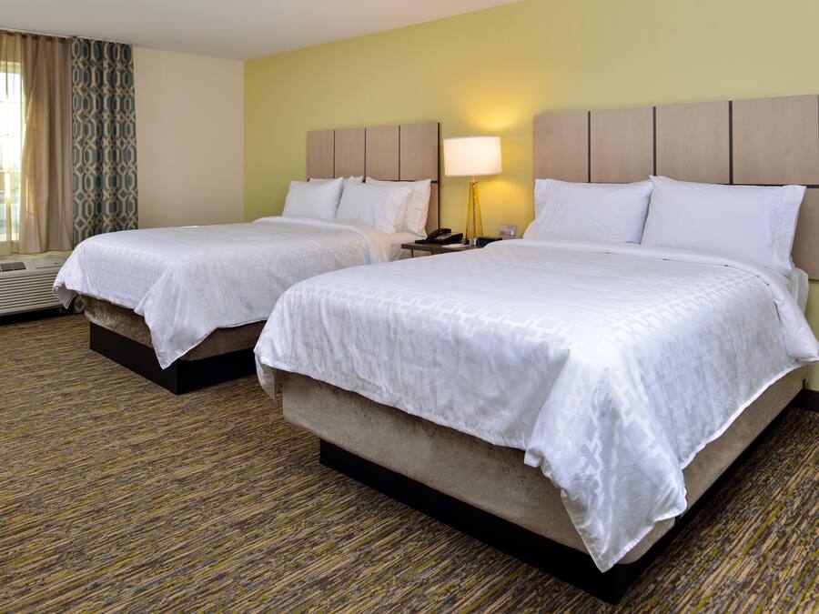 A hotel room with two beds, a bedside table with a lamp, and a window with curtains.