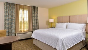 A hotel room with a large bed, a bedside table, a lamp, and a window with curtains. - Candlewood Suites Lodi (Lodi)