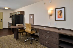 A compact hotel room with a kitchenette, a dining area with a table and chairs, a desk with drawers, and a framed picture on the wall. - Candlewood Suites Lodi (Lodi)