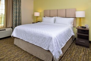A hotel room with a bed, bedside lamps, a heater, and a window with curtains. - Candlewood Suites Lodi (Lodi)