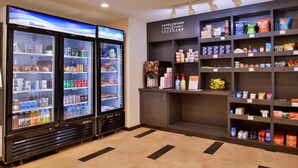 Un área de autoservicio para bebidas con dos refrigeradores Blueair y una alacena Candlewood llena de refrigerios y bebidas.