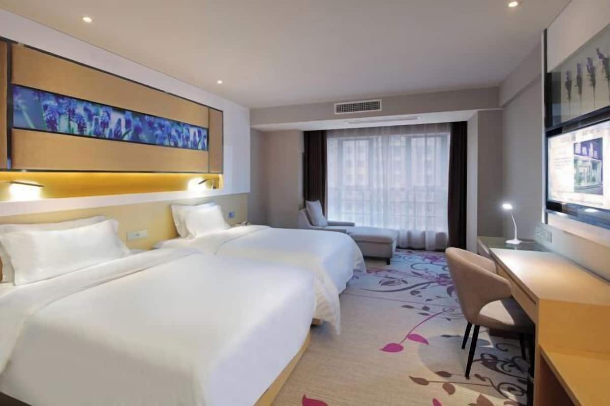 Ein Hotelzimmer mit zwei Betten, einem Schreibtisch, einem Stuhl und einem großen Fenster mit Vorhängen.