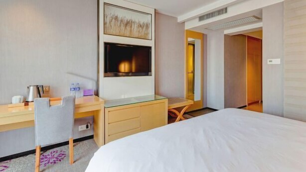 A hotel room with a bed, a desk with a chair, a flat-screen TV, a fireplace, and a door leading to another room. - Lavande Hotels (Xi'an Xibu Avenue Yangguangcheng) (Xi'an)