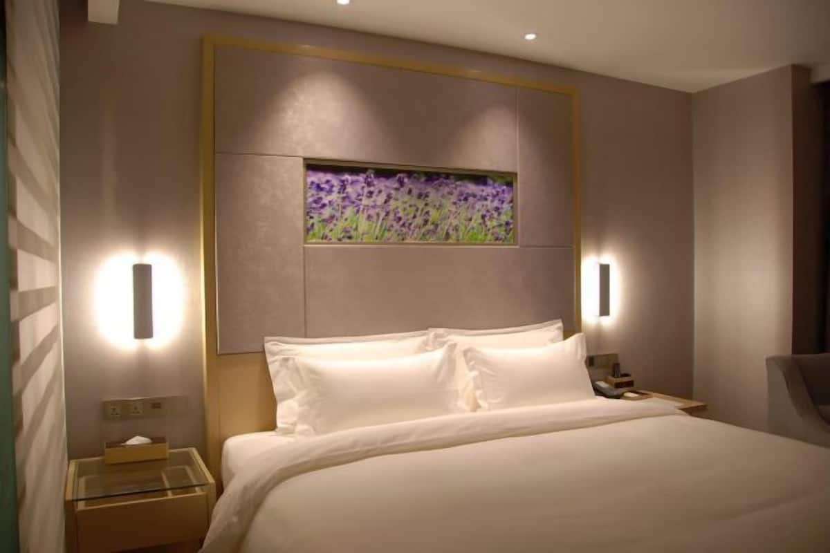 Ein Hotelzimmer mit einem Bett, Nachttischen, einer Wandleuchte und einem floralen Bild in einem Rahmen.
