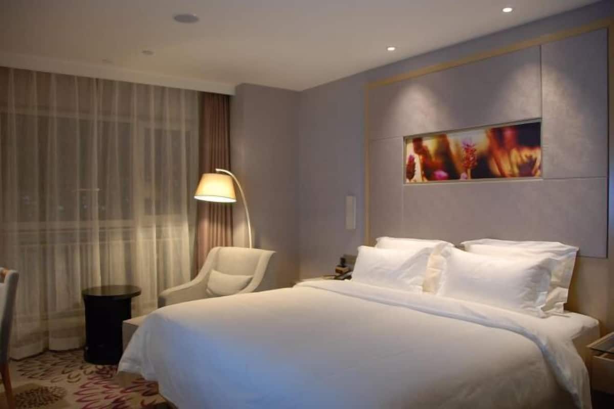 Ein Hotelzimmer mit Bett, Sessel, Lampe und einem Bild an der Wand.