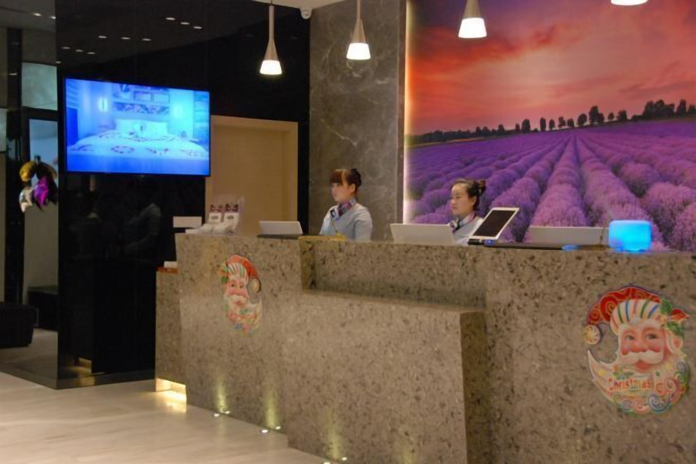 Una recepción con una pantalla de televisión, dos empleados y un gran mural de un campo de lavanda.