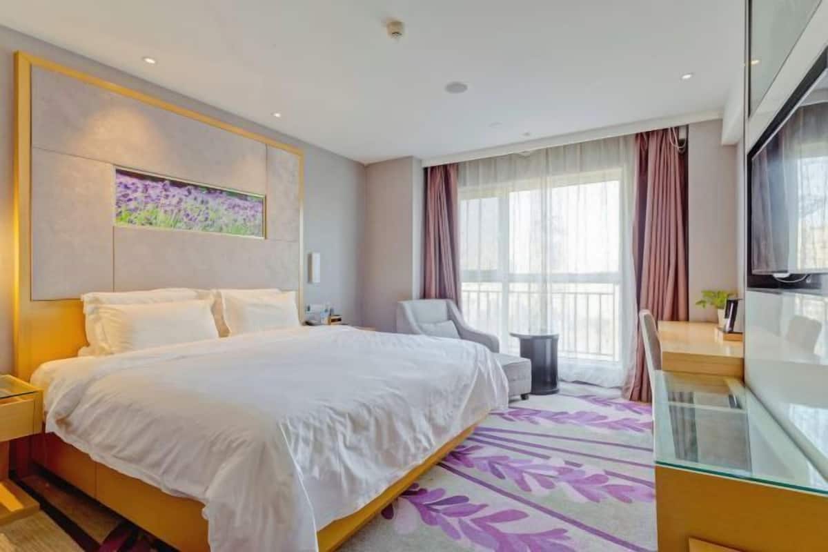 Ein Hotelzimmer mit Bett, Sessel, kleinem Tisch, Fernseher und einem Fenster mit Vorhängen.