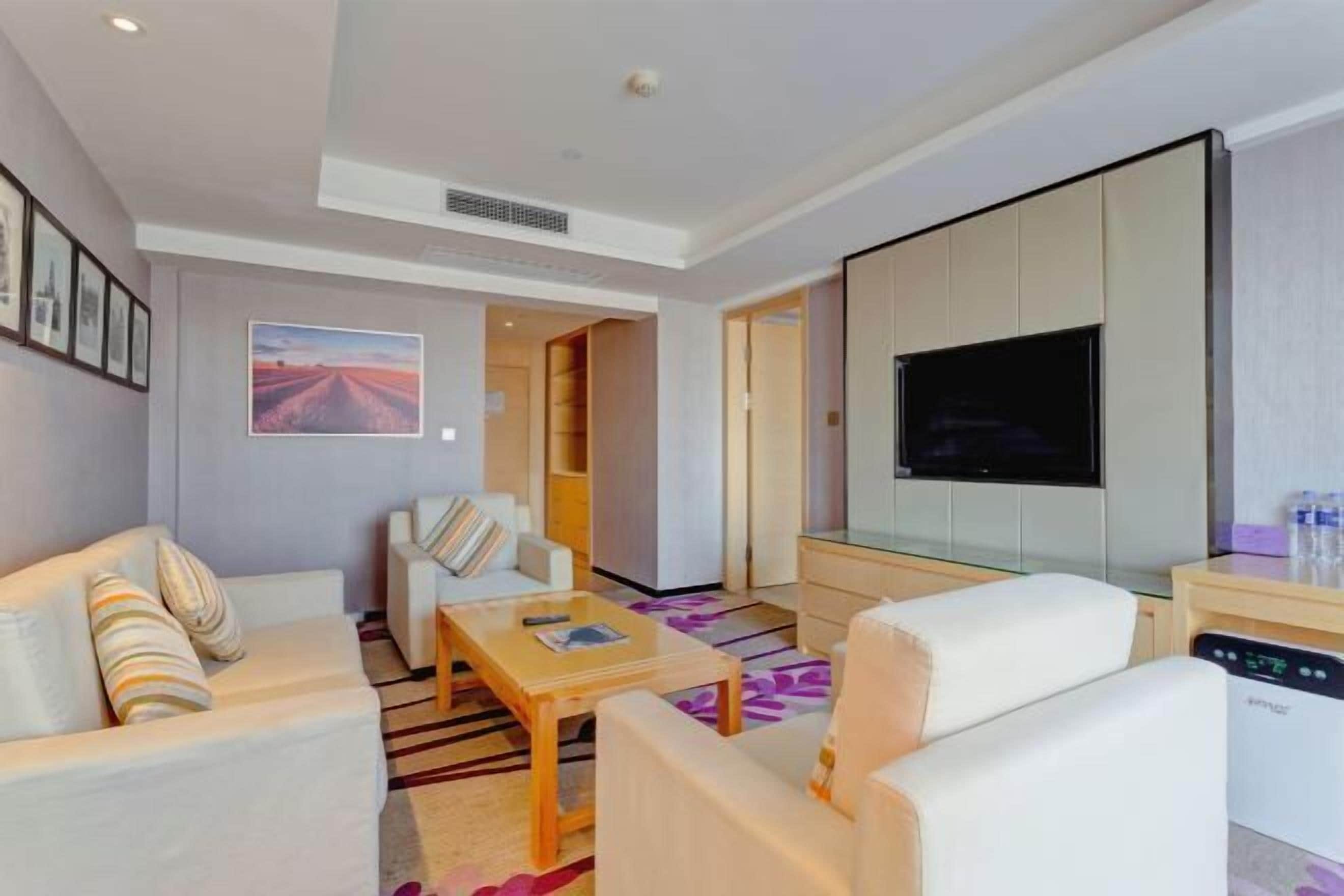 Quarto de hotel moderno com sofá, poltronas, mesa de centro, TV de tela plana e uma janela grande.