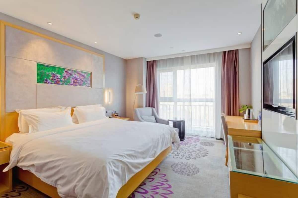 Ein Hotelzimmer mit Bett, Schreibtisch, Stuhl, Fernseher und einem Fenster mit Vorhängen.