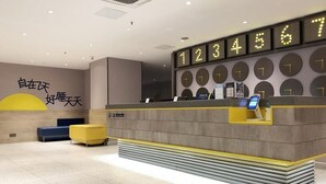 Un espace d’accueil d’hôtel au design moderne, comprenant un comptoir d’accueil, un grand horloge et des coins salon.