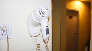 Un sèche-cheveux blanc fixé au mur, avec une prise de courant à proximité et le reflet d’une porte dans un miroir.