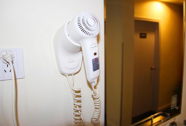 A white hair dryer mounted on a wall with a power outlet and a reflection of a door in a mirror. - 7 Days Inn Chongqing Shapingba High-speed Railway Station (Chongqing)