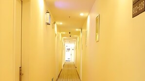 Un couloir d’hôtel avec un sol recouvert de moquette, une porte au fond et un panneau indiquant un numéro de téléphone sur le mur.