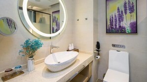Ein modernes Badezimmer mit rundem Spiegel, einem Aufsatzwaschbecken, einer Toilette und einem gerahmten Blumenbild an der Wand.