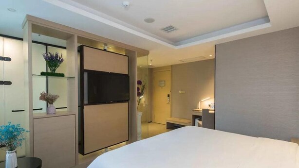 Ein modernes Hotelzimmer mit einem großen Bett, einem Flachbildfernseher, einem kleinen Tisch mit Blumen und einem begehbaren Kleiderschrank.