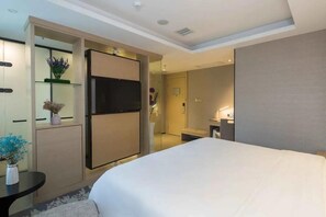Une chambre d’hôtel moderne dotée d’un grand lit, d’un téléviseur à écran plat, d’une petite table agrémentée d’un vase de fleurs et d’un dressing.
