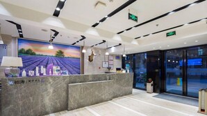 Ein moderner Hotel-Empfangsbereich mit einer Marmor-Theke, einem großen Wandbild einer Landschaft und einem Glastür-Eingang.