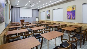 Ein Konferenzraum mit Reihen aus Holztischen und -stühlen, einer Projektionsleinwand und Kunstwerken an den Wänden.