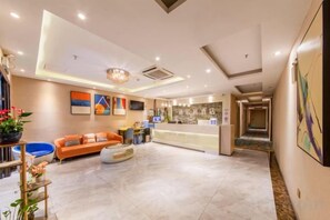 A hotel lobby with a reception desk, seating area, and a staircase leading to other floors.