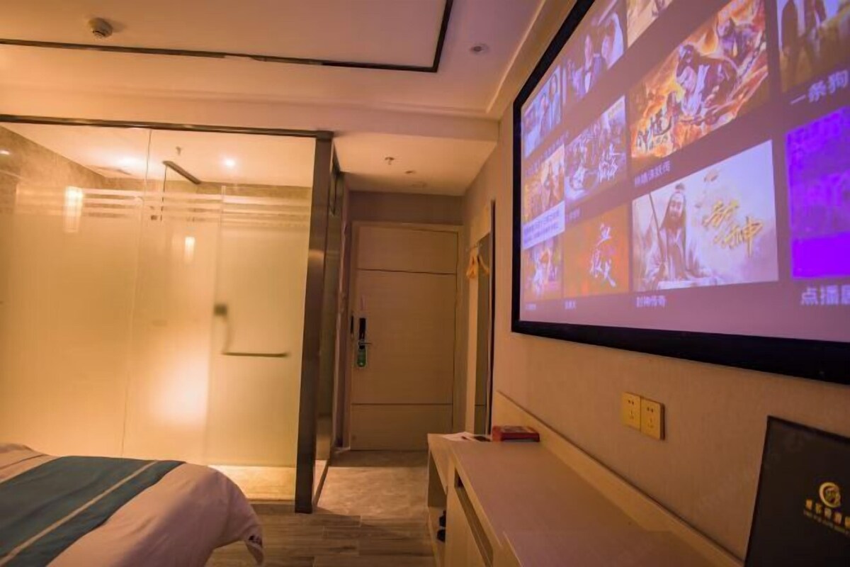 A hotel room with a bed, a shower area, and a wall-mounted TV displaying various images.