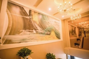 Un hall d’hôtel agrémenté d’un grand tableau abstrait, d’un lustre et de plantes en pot.
