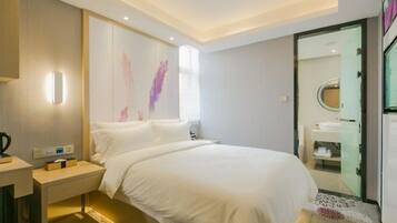 A modern hotel room with a large bed, bedside table, and a bathroom visible through an open door.