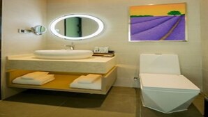 A modern bathroom with a round mirror, a sink, a toilet, and a painting of lavender fields on the wall. - Lavande Hotel (Wuhan)