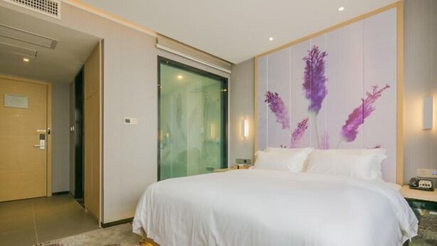 A hotel room with a large bed, a glass door, and a wall with a floral painting. - Lavande Hotel (Wuhan)