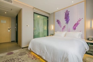 Une chambre d’hôtel avec un grand lit, une porte en verre et un mur orné d’un tableau représentant des motifs floraux.