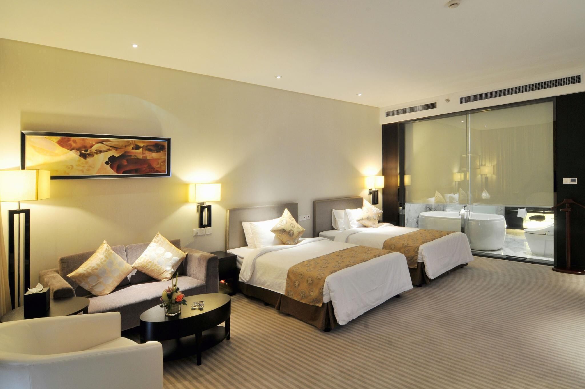 A hotel room with two beds, a sofa, a coffee table, and a large window with a view of the bathroom.