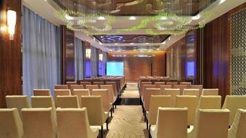 A conference room with rows of chairs facing a screen, wooden paneling, and decorative ceiling elements.