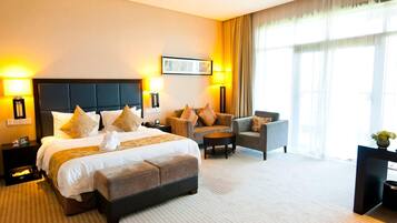 A hotel room with a large bed, two armchairs, a small table, and a desk with a lamp.