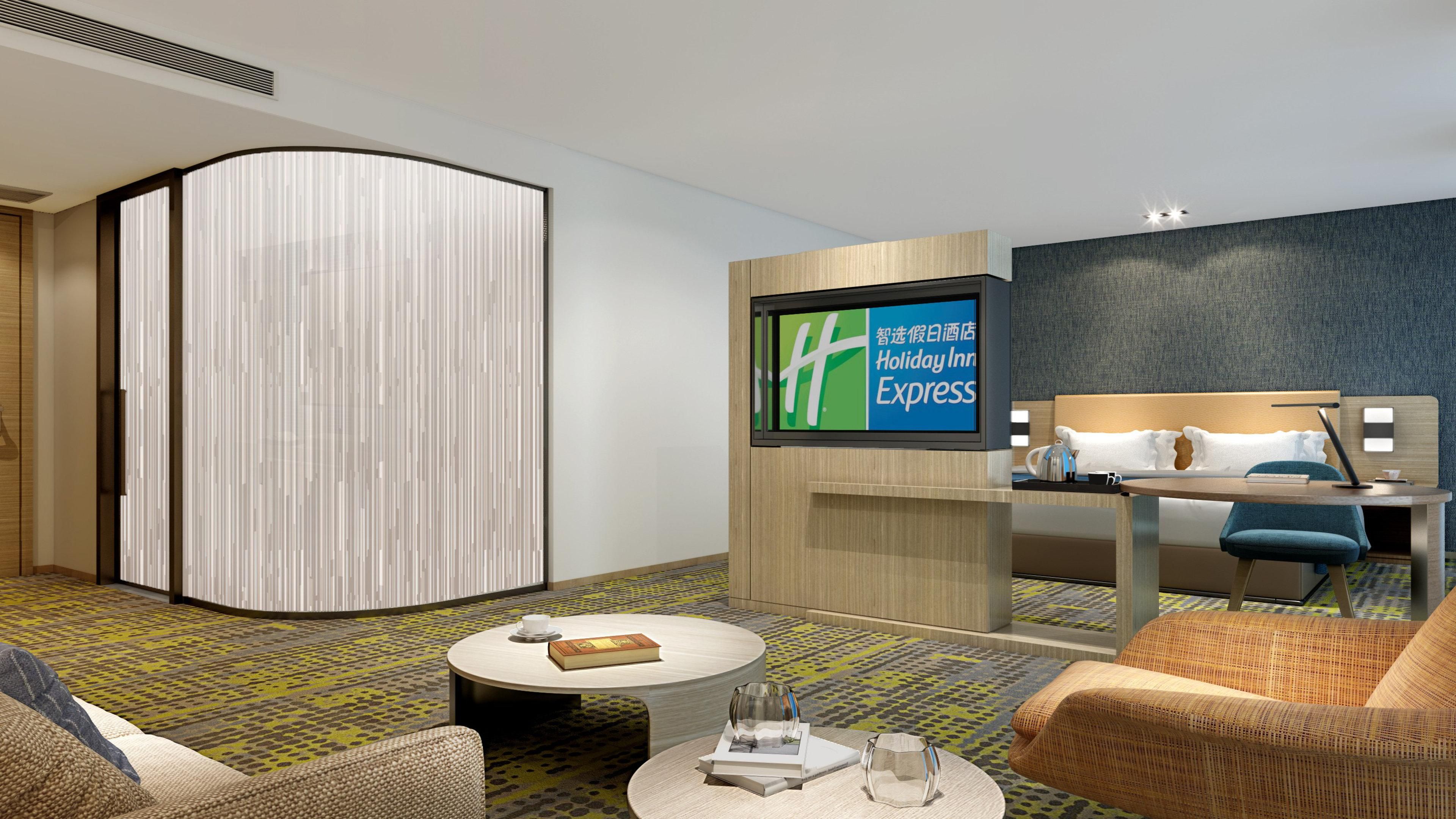 A modern hotel room with a bed, a TV, a seating area with a coffee table, and a patterned carpet.