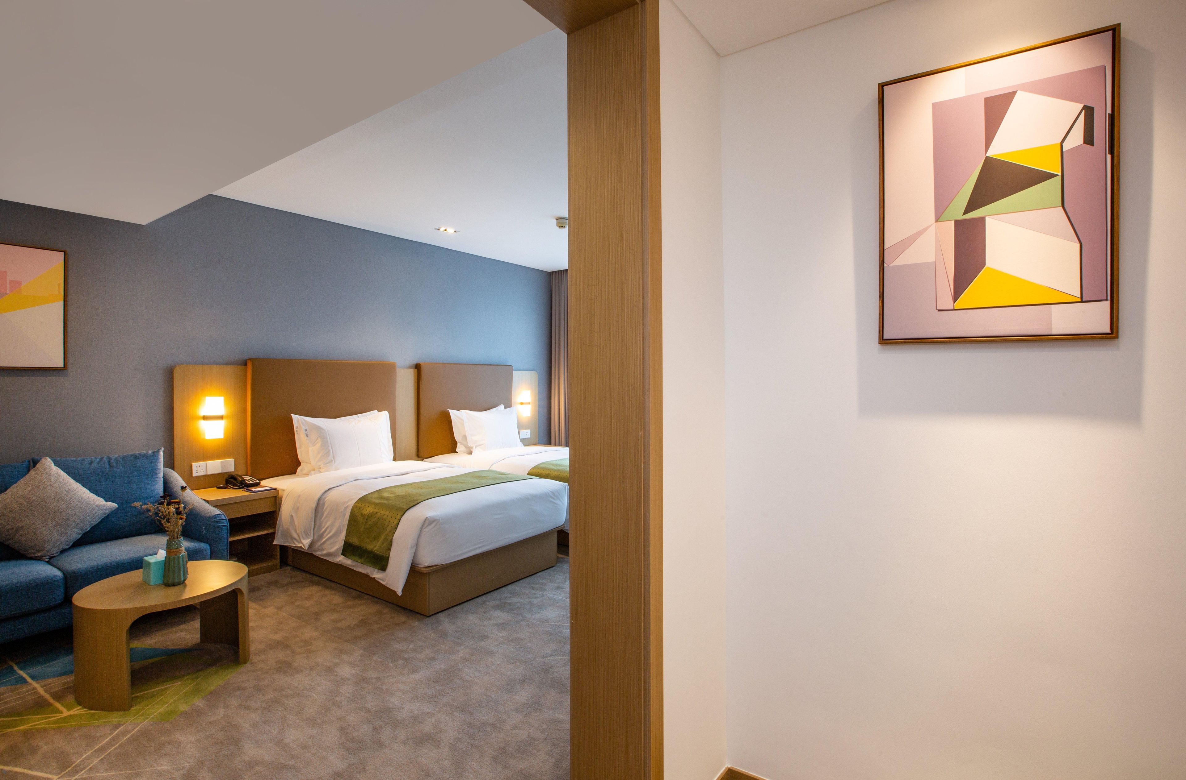 Una habitación de hotel con cama, sofá, mesita de noche y un cuadro en la pared.