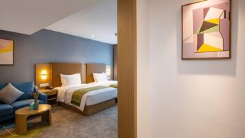 Una habitación de hotel con cama, sofá, mesita de noche y un cuadro en la pared.