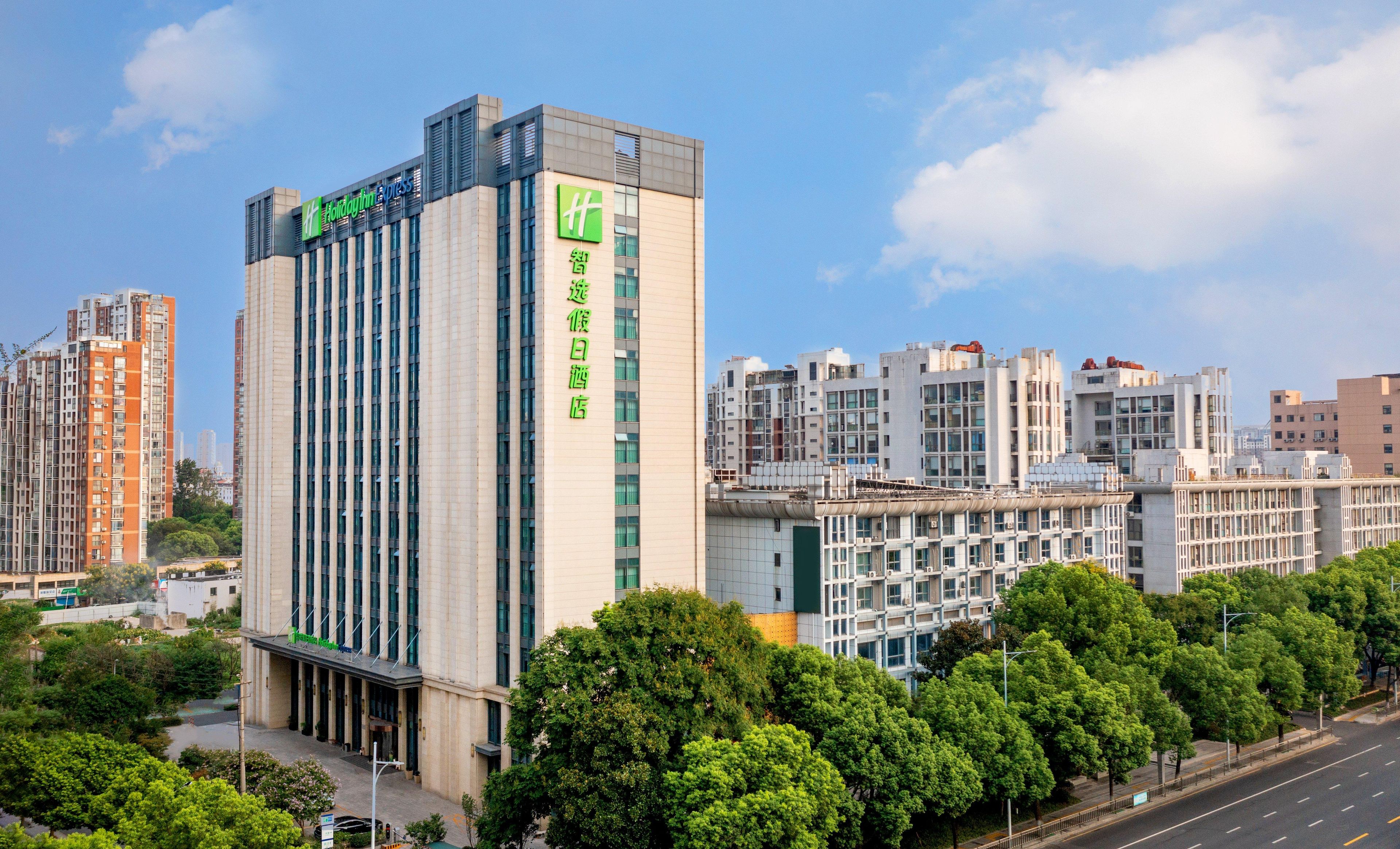 A modern hotel with a prominent green logo, multiple floors, and a central courtyard with trees.
