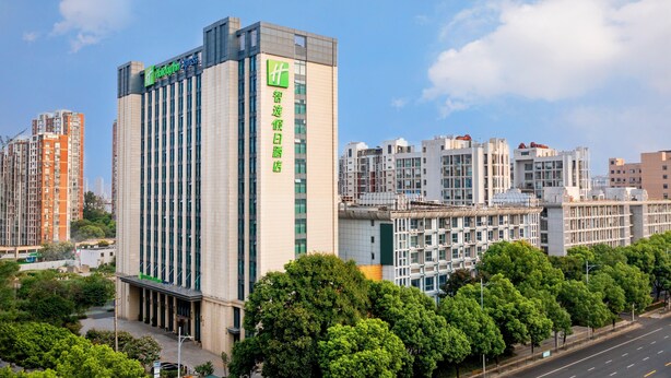 Un hotel moderno con un llamativo logo verde, varios pisos y un patio central con árboles.