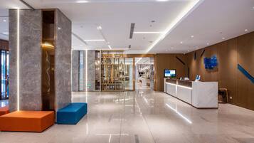 Un moderno vestíbulo de hotel con una recepción, zonas de estar y un separador de vidrio que conduce a un restaurante.